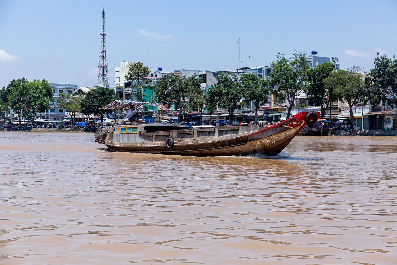 Traditional hand-rowed wooden sampan navigating a narrow lush water-coconut canal in the Mekong Delta